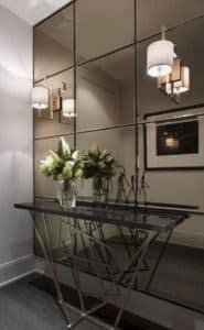 Hall de entrada com aparador inox e parede com espelho bronze.